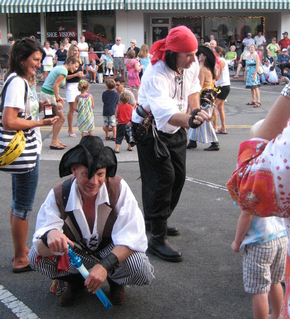 Two men dressed as pirates interact with children at a lively street event.