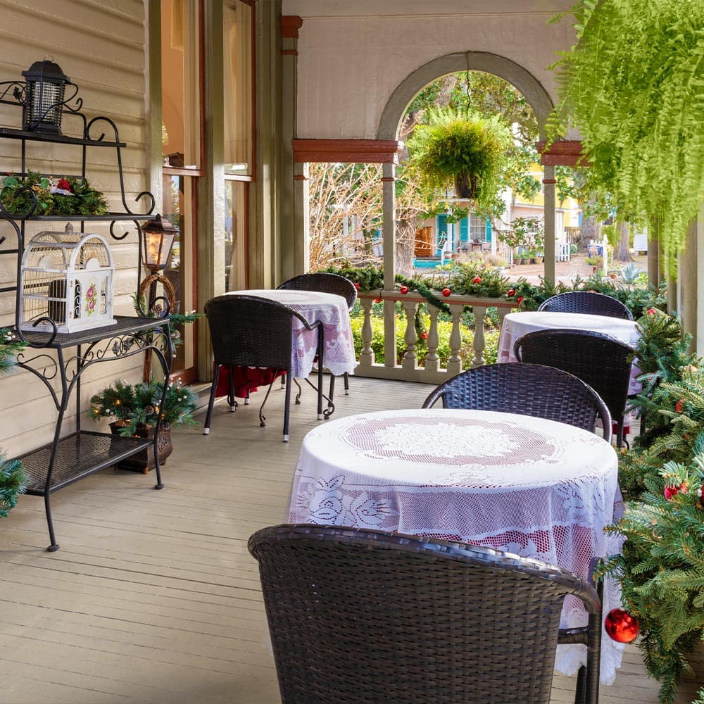 A cozy porch with decorated tables and chairs, adorned with greenery and festive accents.
