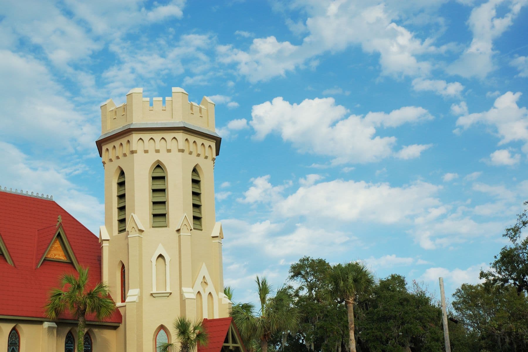 A castle-like church tower stands against a bright blue sky with scattered clouds.
