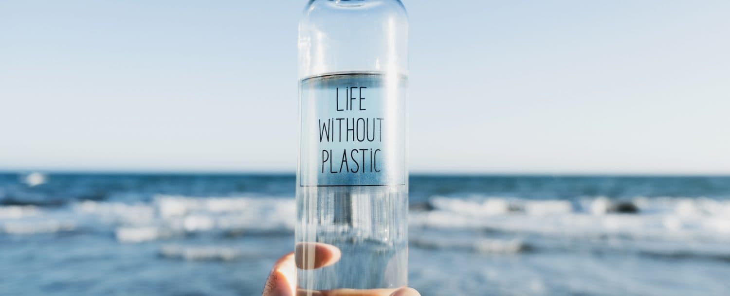 A clear bottle labeled "Life Without Plastic" is held against a backdrop of the ocean.