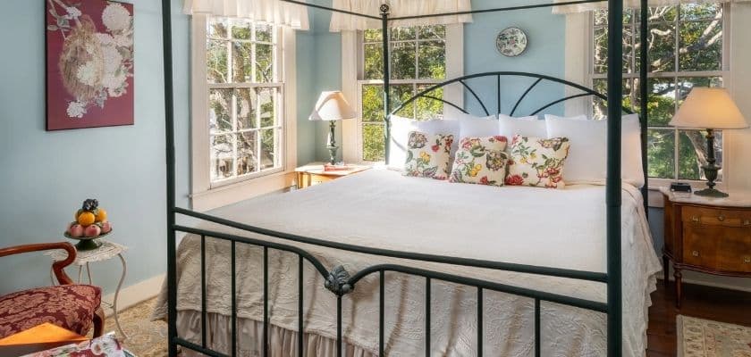 A cozy bedroom featuring a four-poster bed, large windows, and decorative pillows.