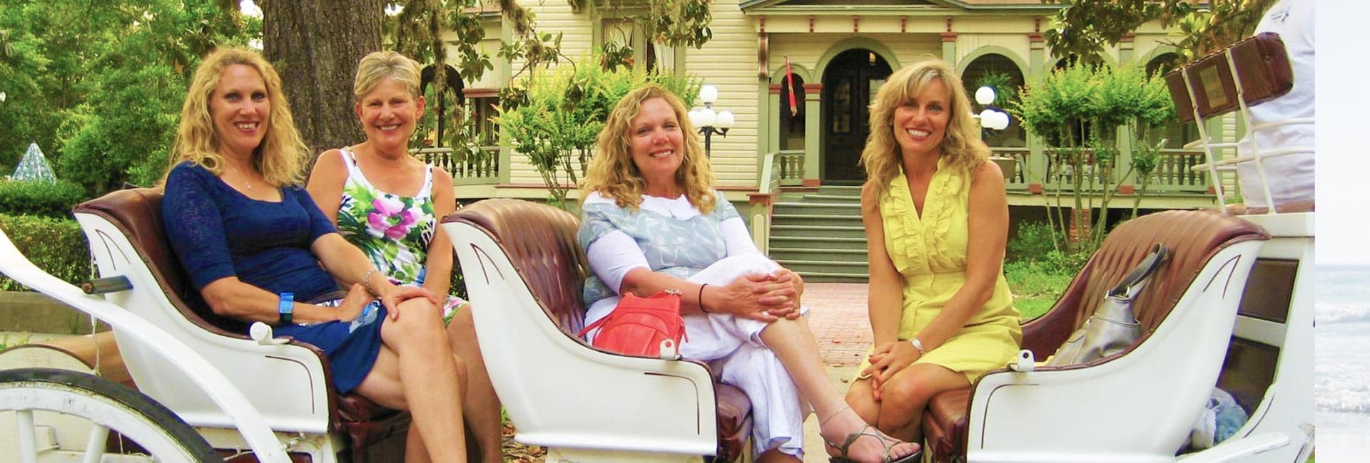 Four women seated in a horse-drawn carriage in a park-like setting.