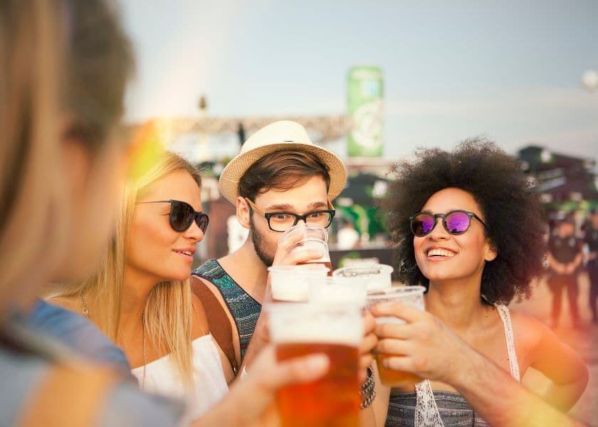 A group of friends clinking glasses of beer together outdoors at a lively event. A group of friends clinking glasses of beer together outdoors at a lively event.