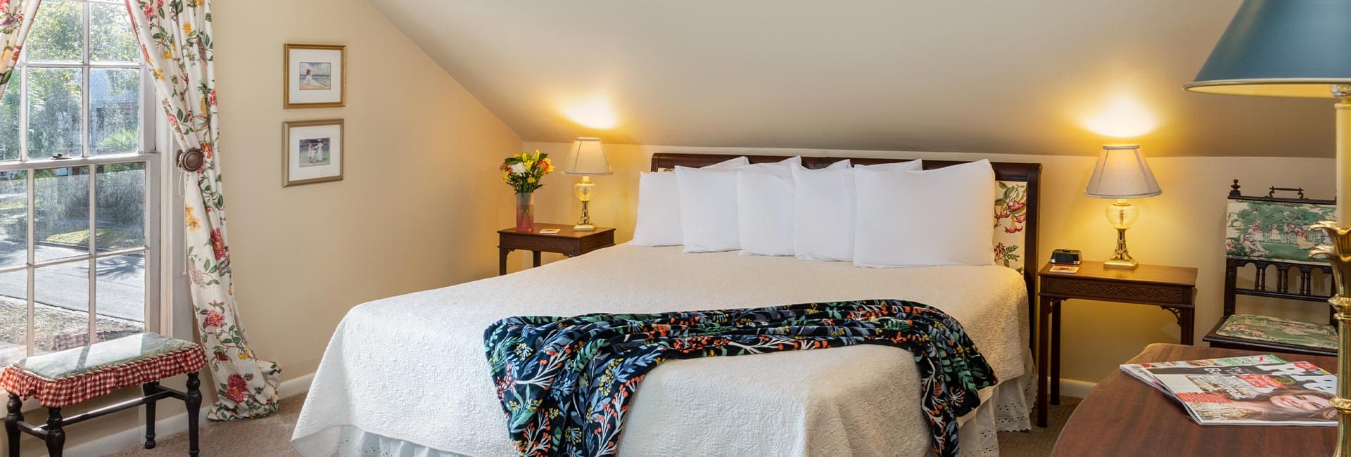A cozy bedroom featuring a large bed, floral curtains, and warm lighting.