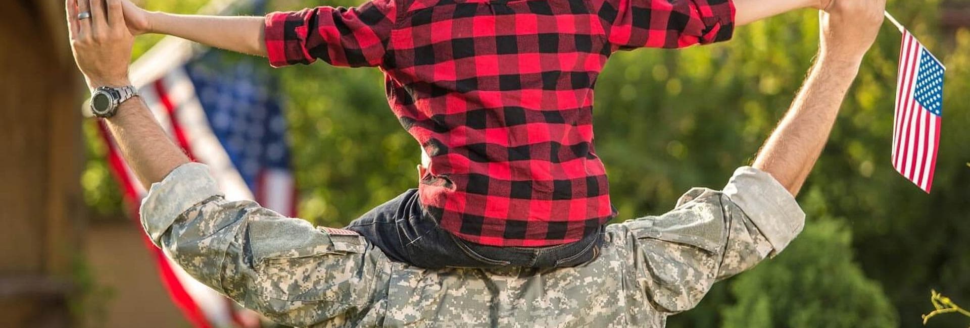 A soldier lifts a child on their shoulders while holding an American flag.