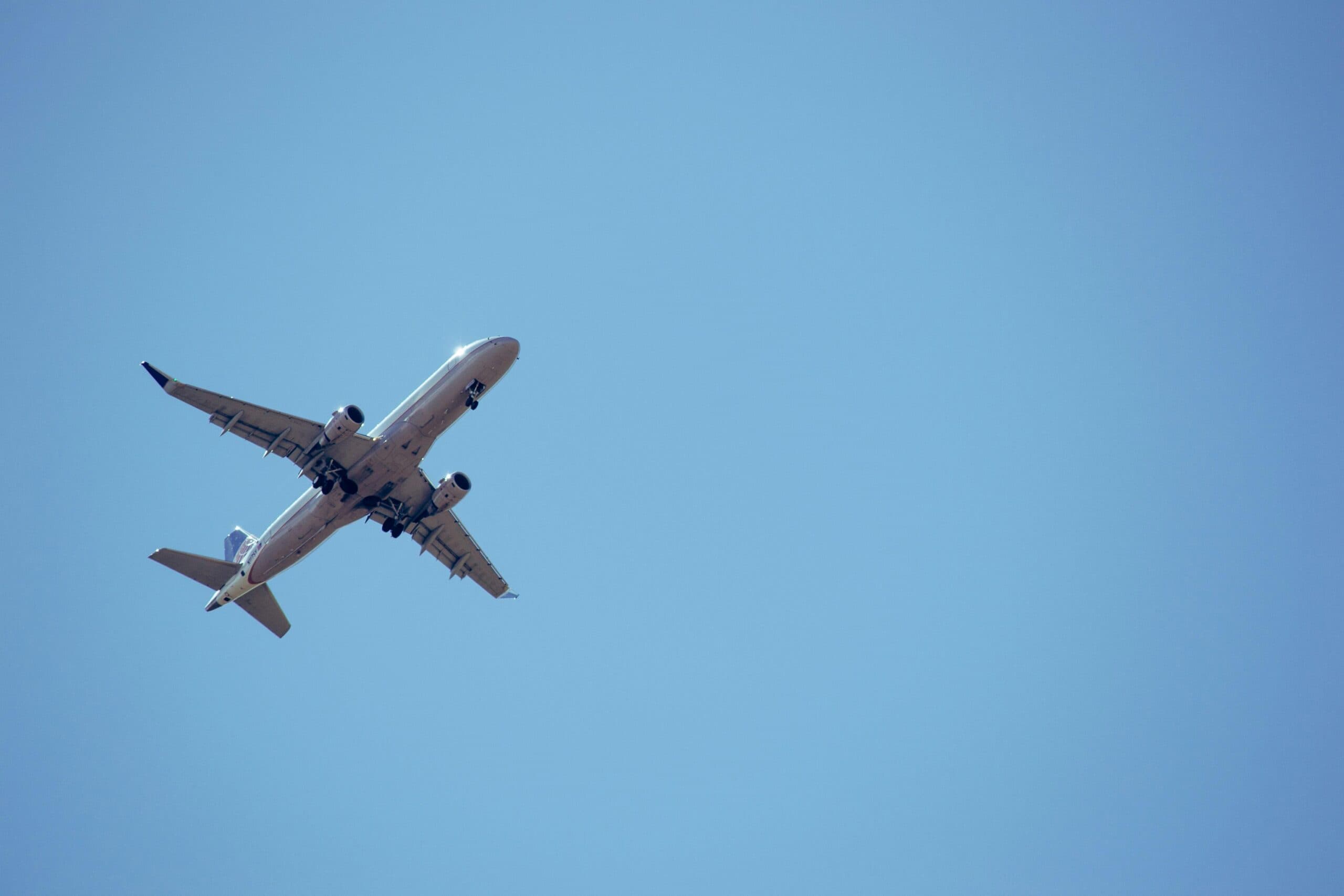 An airplane flies overhead against a clear blue sky. An airplane flies overhead against a clear blue sky.
