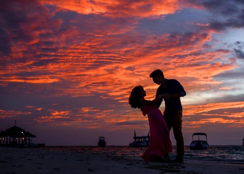 A couple dances on the beach at sunset, silhouetted against a vibrant, colorful sky. A couple dances on the beach at sunset, silhouetted against a vibrant, colorful sky.