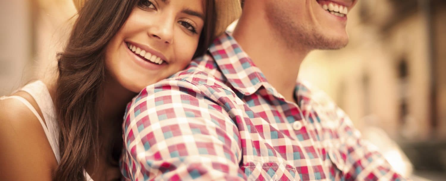 A smiling couple sits close together, enjoying a sunny day.