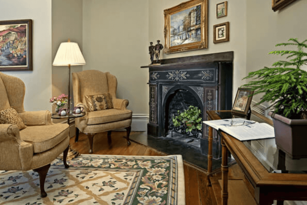 Cozy sitting area featuring two armchairs, a decorative fireplace, artwork, and a small table with plants.