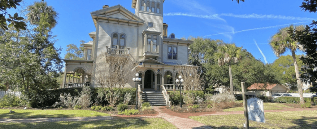 Historic Victorian house surrounded by lush greenery and a clear blue sky.