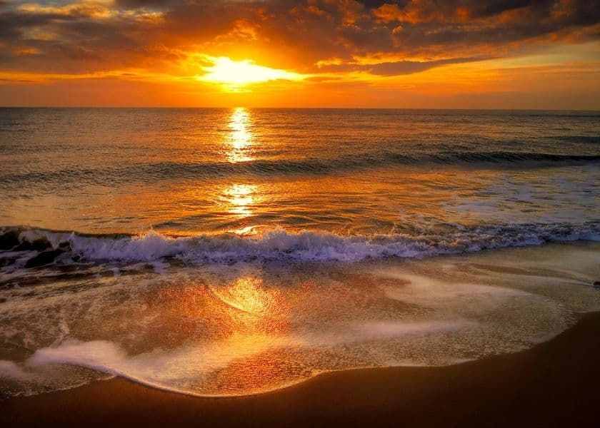 Sunset over a serene ocean, with gentle waves lapping the shore.