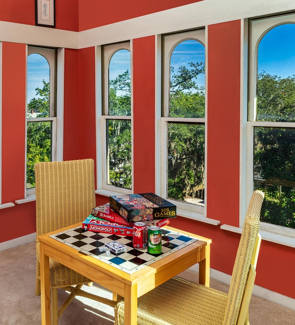A cozy corner with a game table, surrounded by windows and filled with board games.