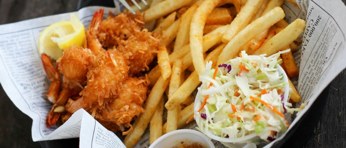 A basket of crispy fried shrimp, French fries, and coleslaw with a lemon wedge.