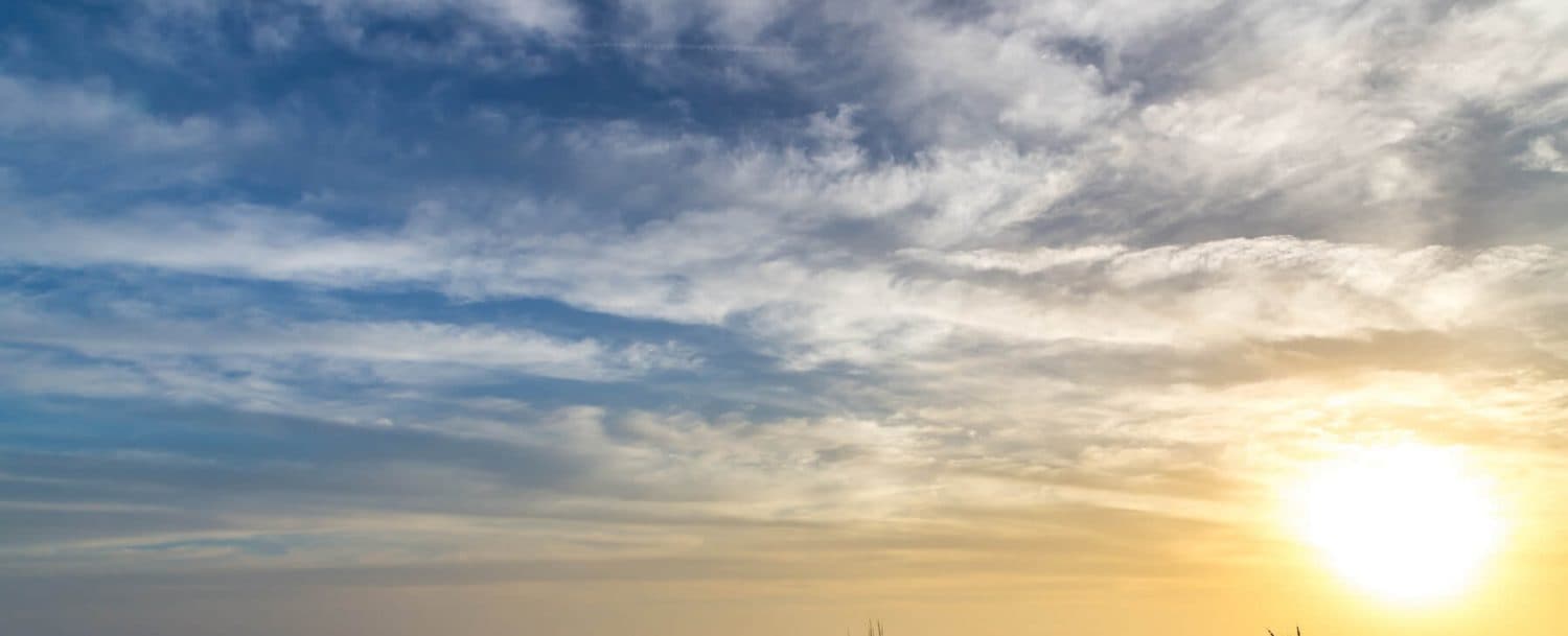 A vibrant sunset casts warm hues across a partly cloudy sky.