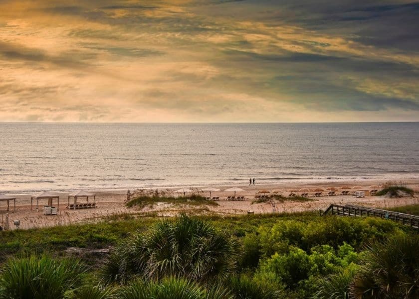A tranquil beach scene at sunset with a couple walking along the shore.