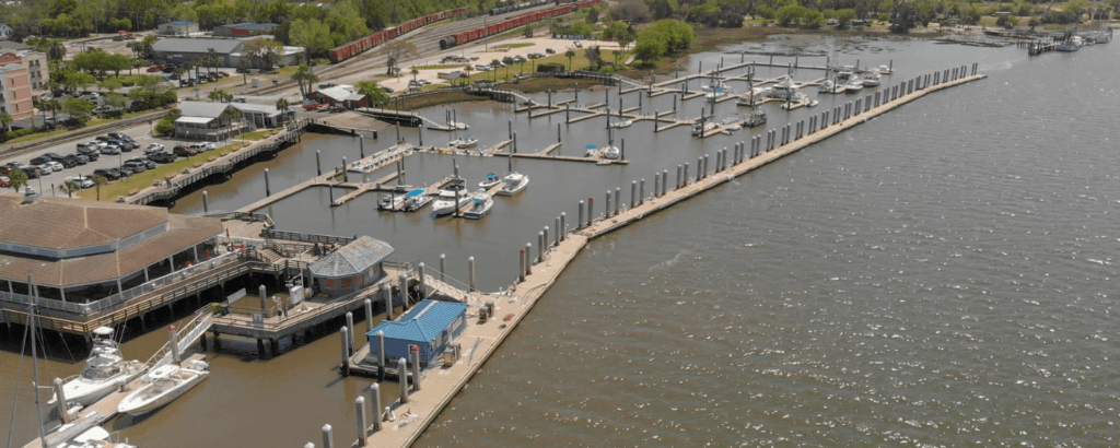 Aerial view of a marina with boats docked, featuring a waterfront restaurant and surrounding greenery.