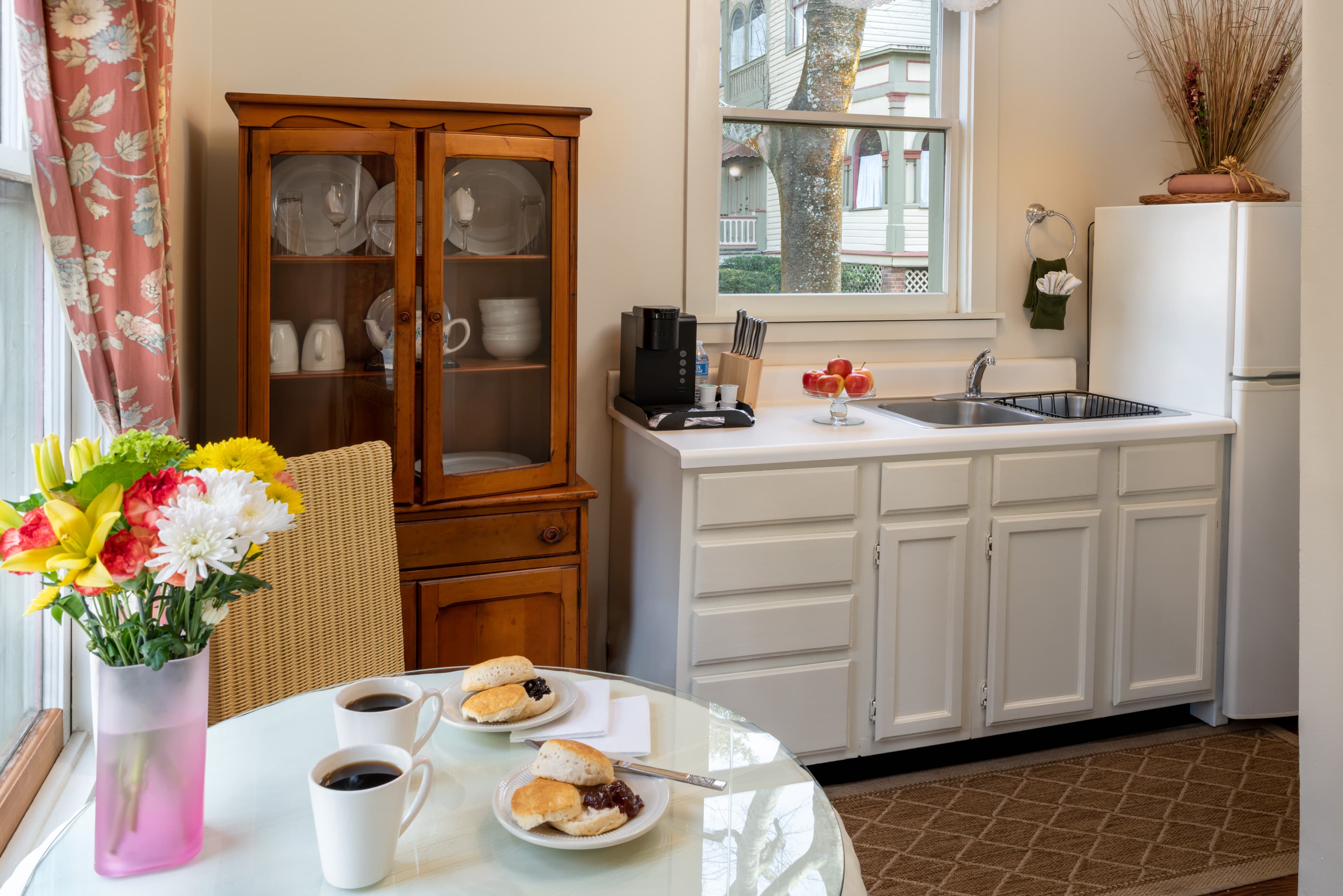 Charming kitchenette and dining area featuring a breakfast table, coffee station, mini refrigerator, farmhouse-style cabinetry, and hardwood floors