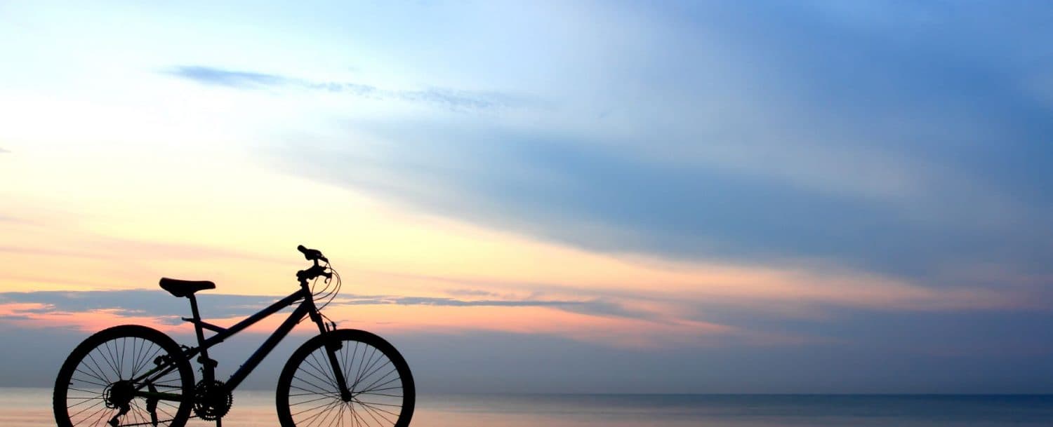Silhouette of a bicycle against a colorful sunset sky over the ocean.