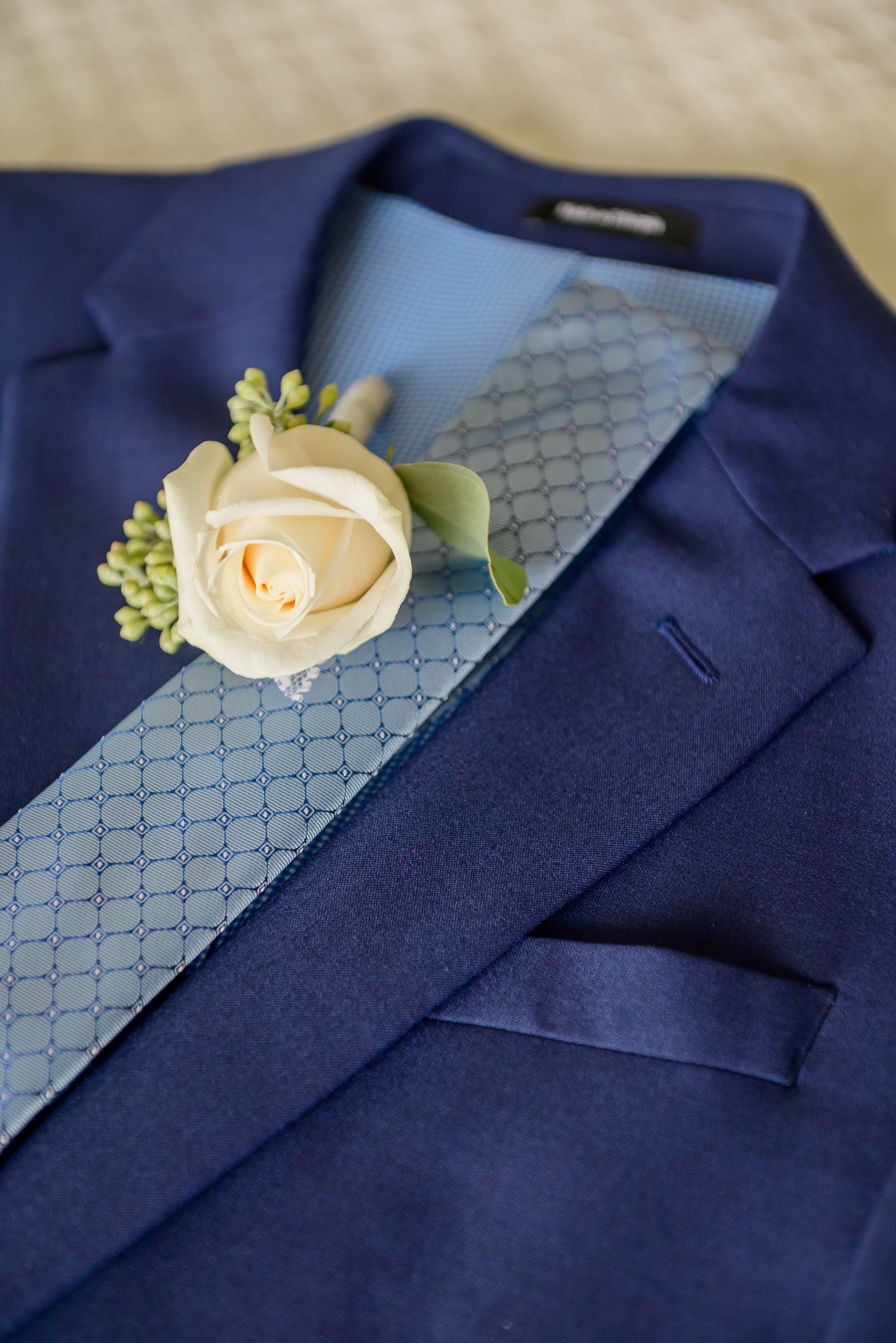 A navy suit jacket with a light blue tie and a white rose boutonnière.