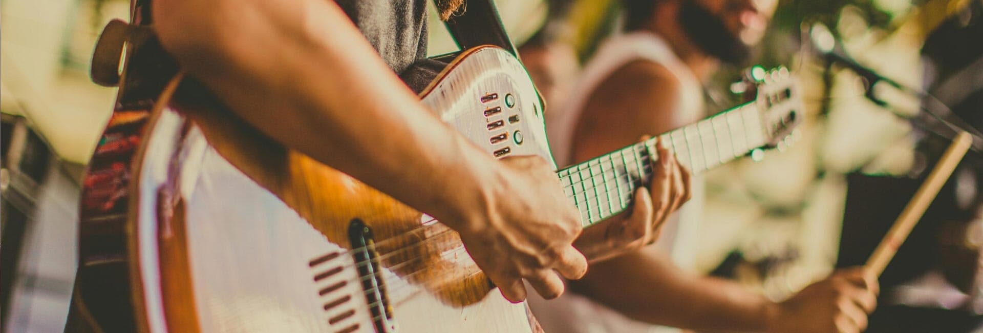 A close-up of a musician's hand playing a guitar in a band setting.