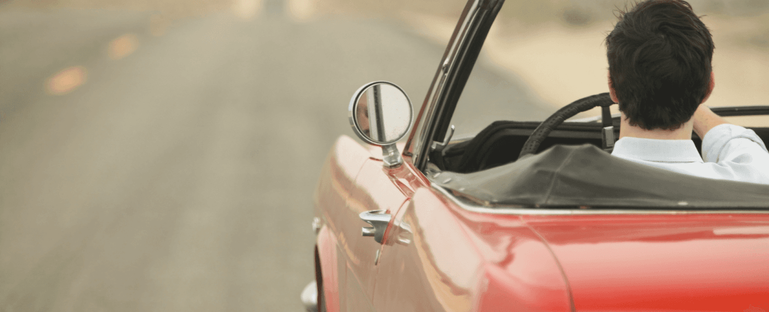 A person drives a red convertible down a deserted road.