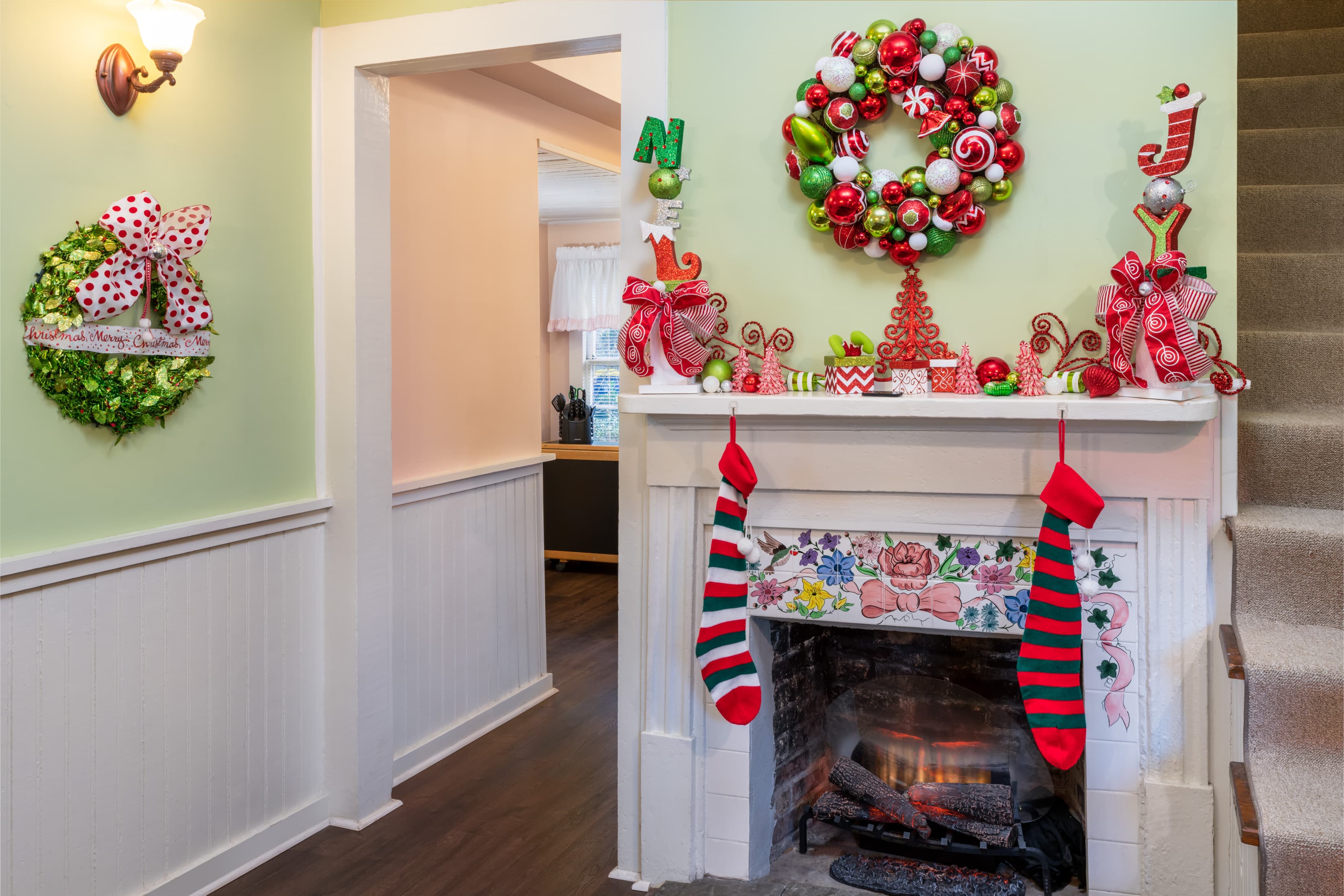 Festively decorated cottage fireplace featuring colorful Christmas wreaths, stockings, holiday décor, and a cozy seasonal atmosphere.