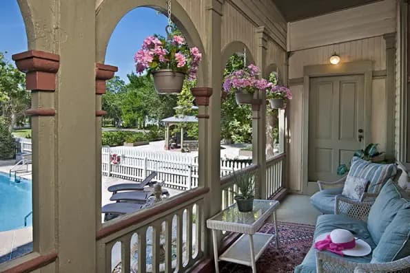 A cozy porch with potted flowers overlooks a pool and patio area.