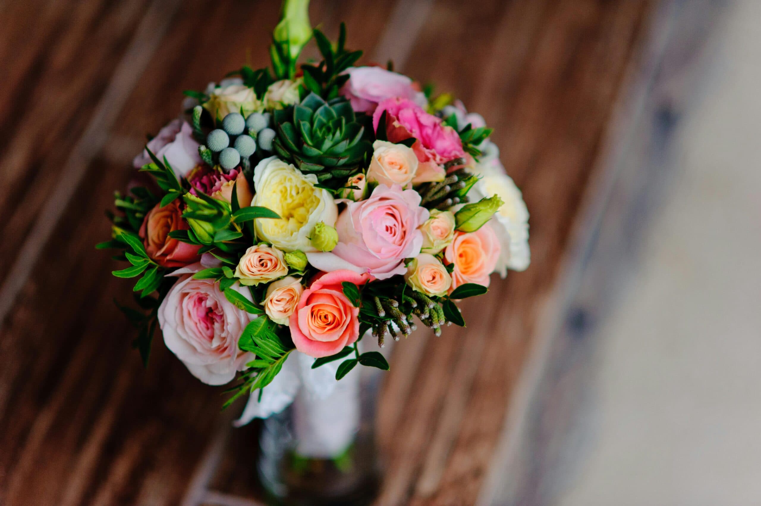 A colorful bouquet of roses and succulents arranged in a glass vase on a wooden surface.