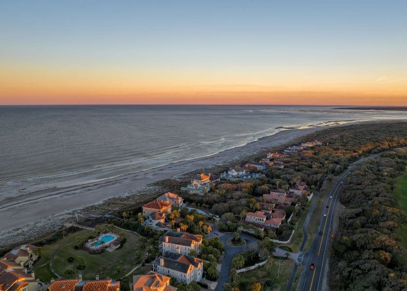 Aerial view of a coastal area with houses, a road, and a sunset over the ocean. Aerial view of a coastal area with houses, a road, and a sunset over the ocean.