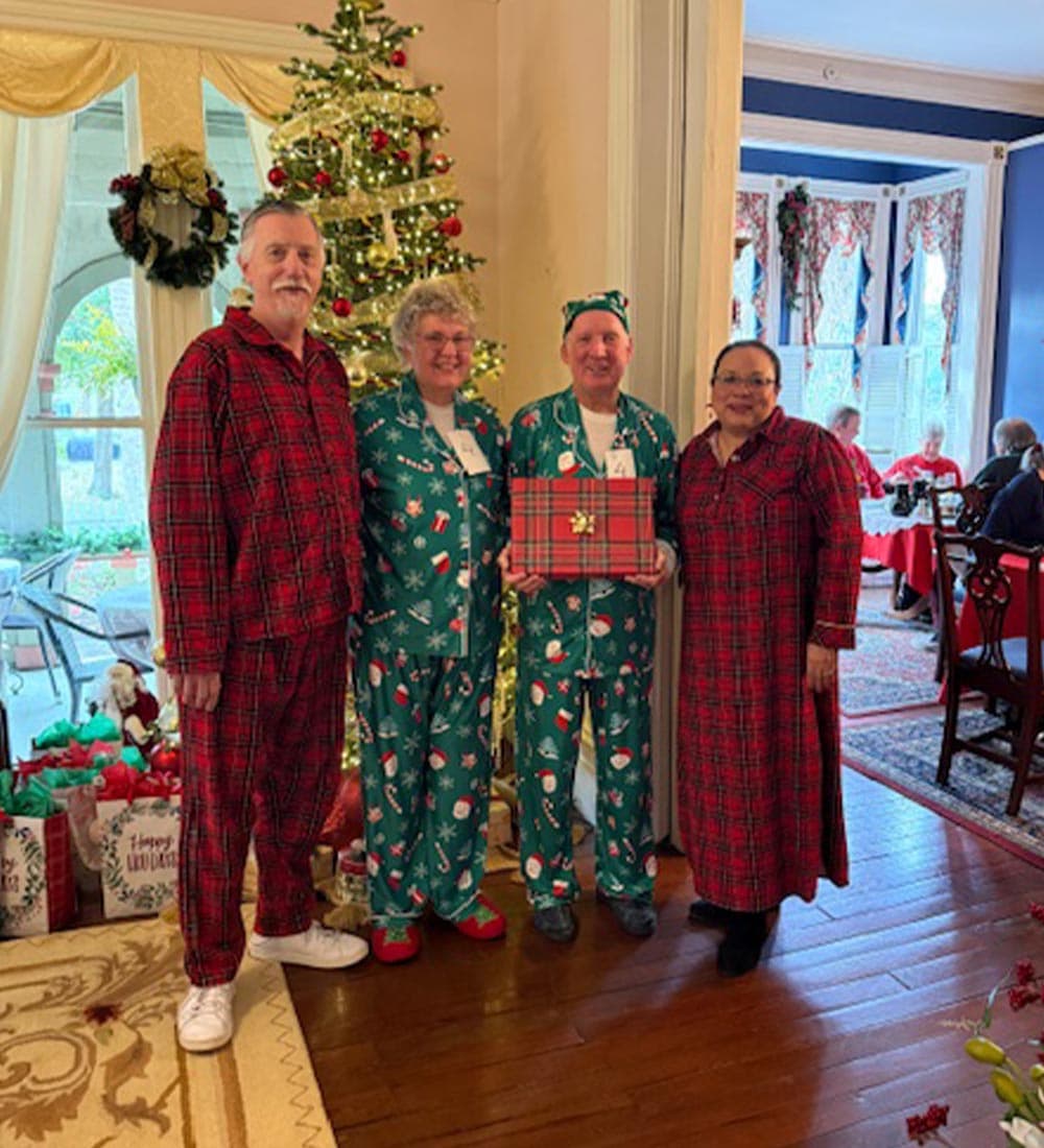 Four people in festive pajamas pose together in front of a Christmas tree.