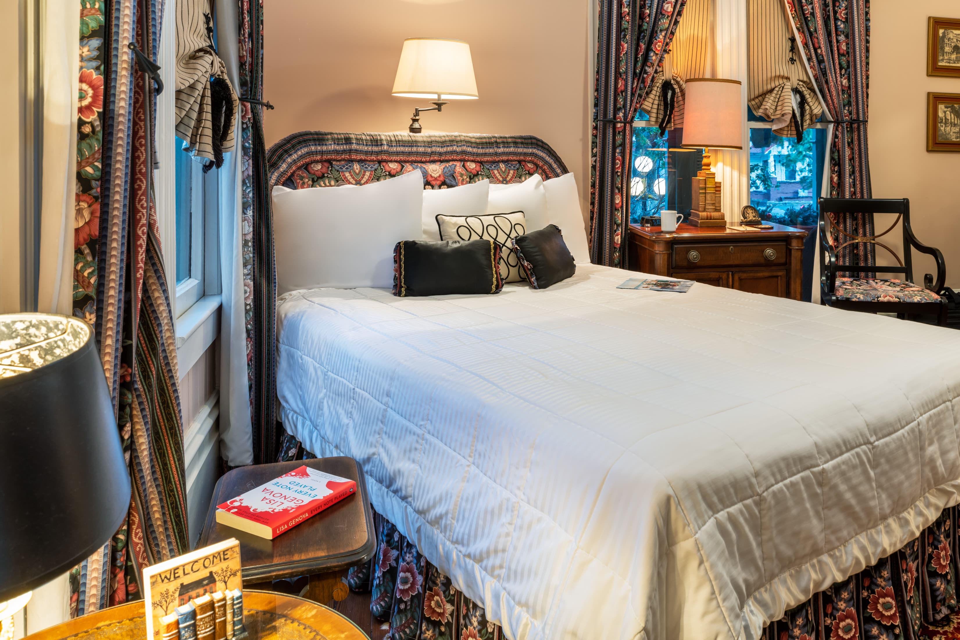 Cozy queen bedroom featuring plush bedding, antique wood furniture, warm lighting, and elegant Victorian-inspired décor.