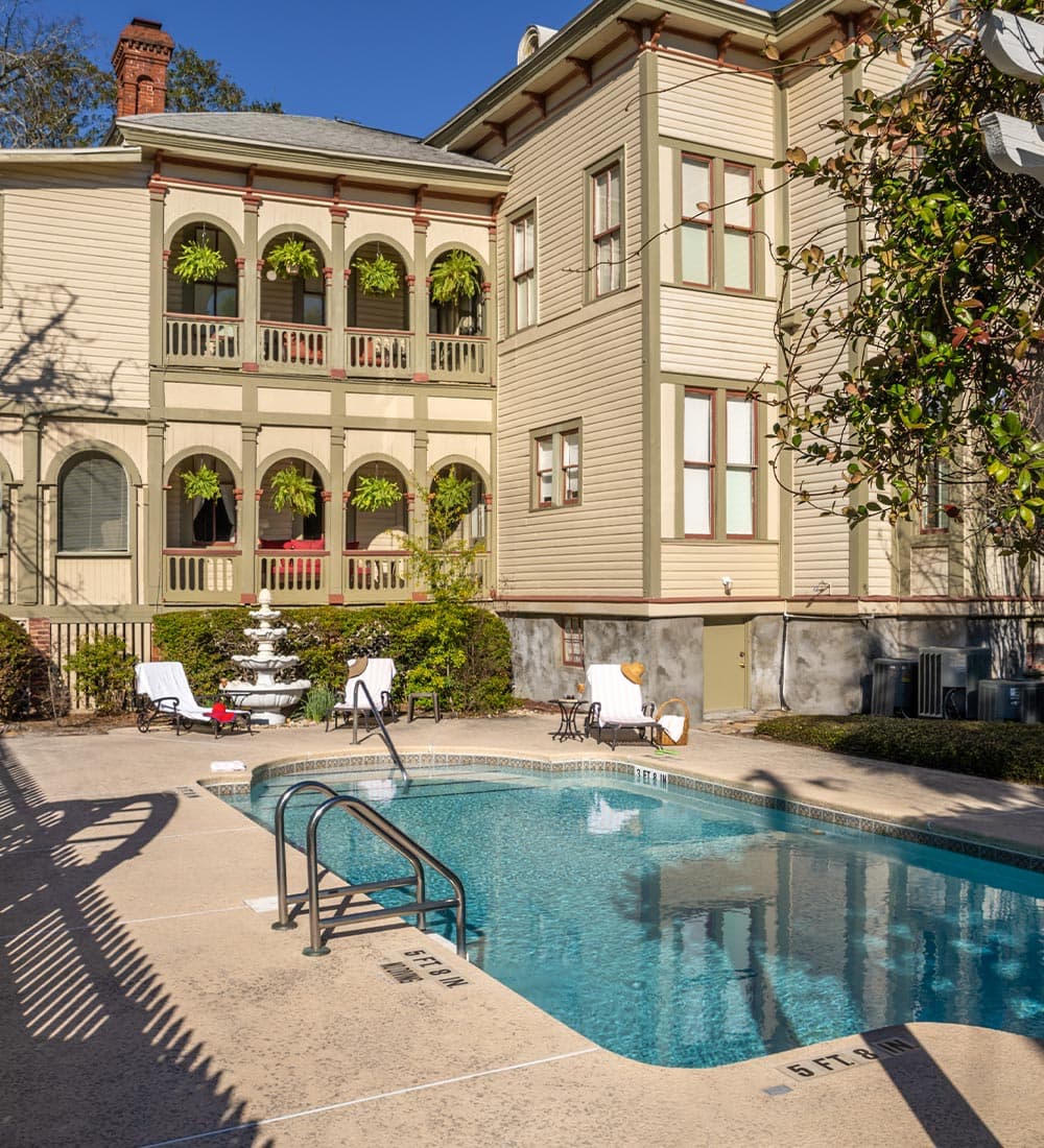 A tranquil pool area surrounded by a charming, historic building with balconies adorned by hanging plants.