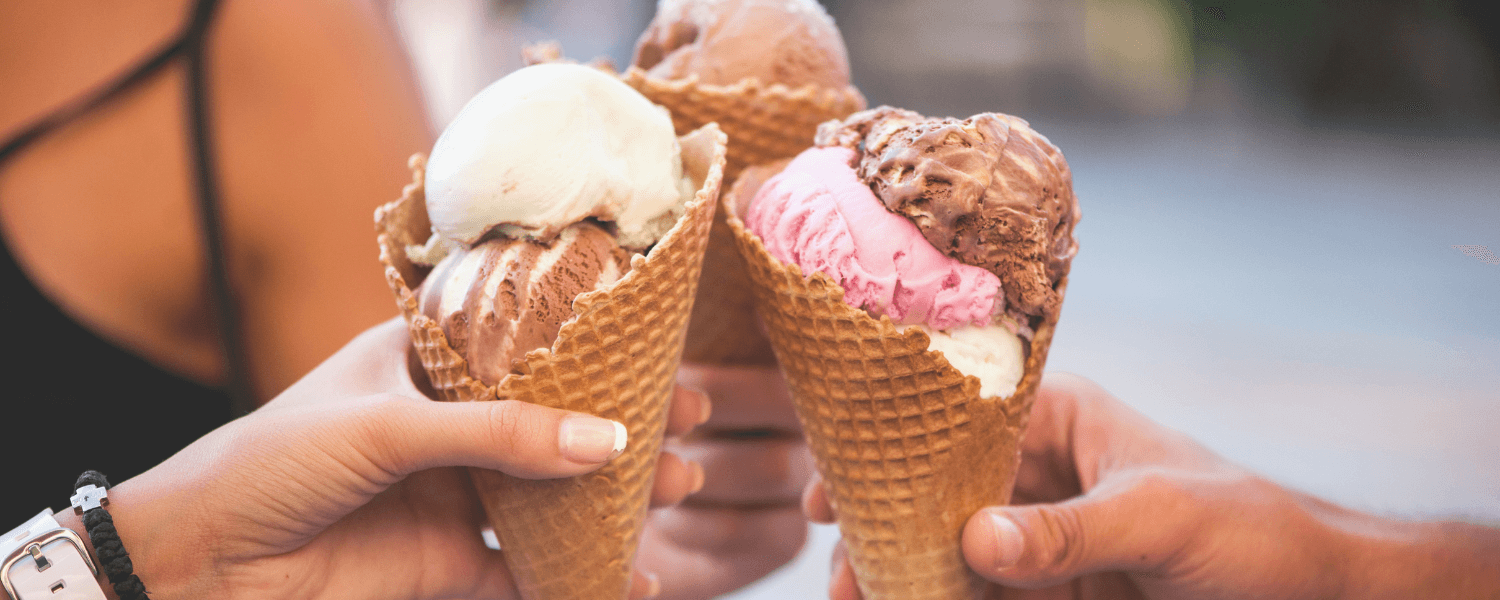 Three ice cream cones are raised in a toast, showing flavors of chocolate, mint, and strawberry.