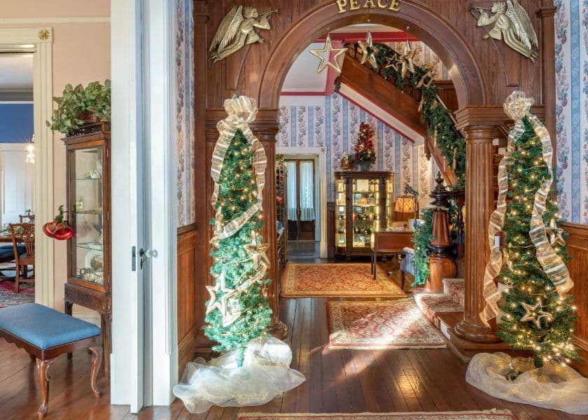 A decorated entryway features two Christmas trees and elegant wooden architecture.