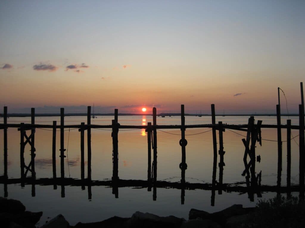 A serene sunset over calm waters, framed by silhouetted wooden posts.