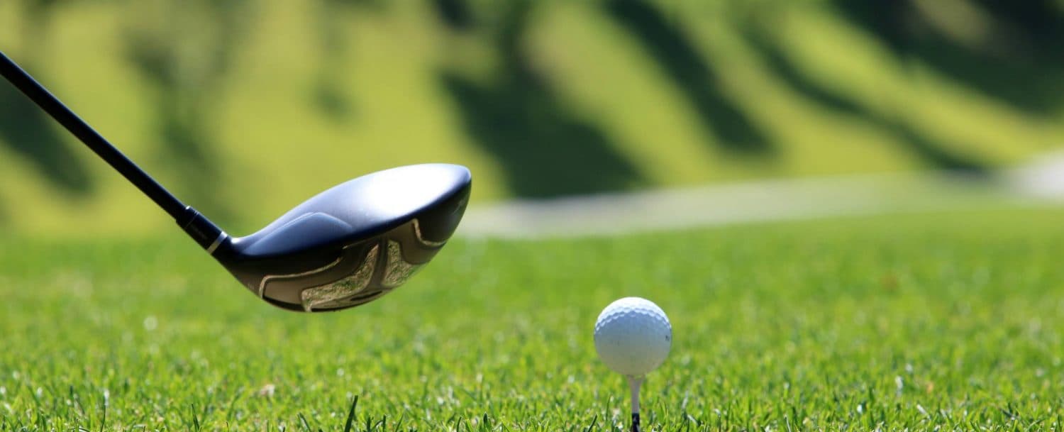 A golf club is poised above a white golf ball on a grassy fairway.