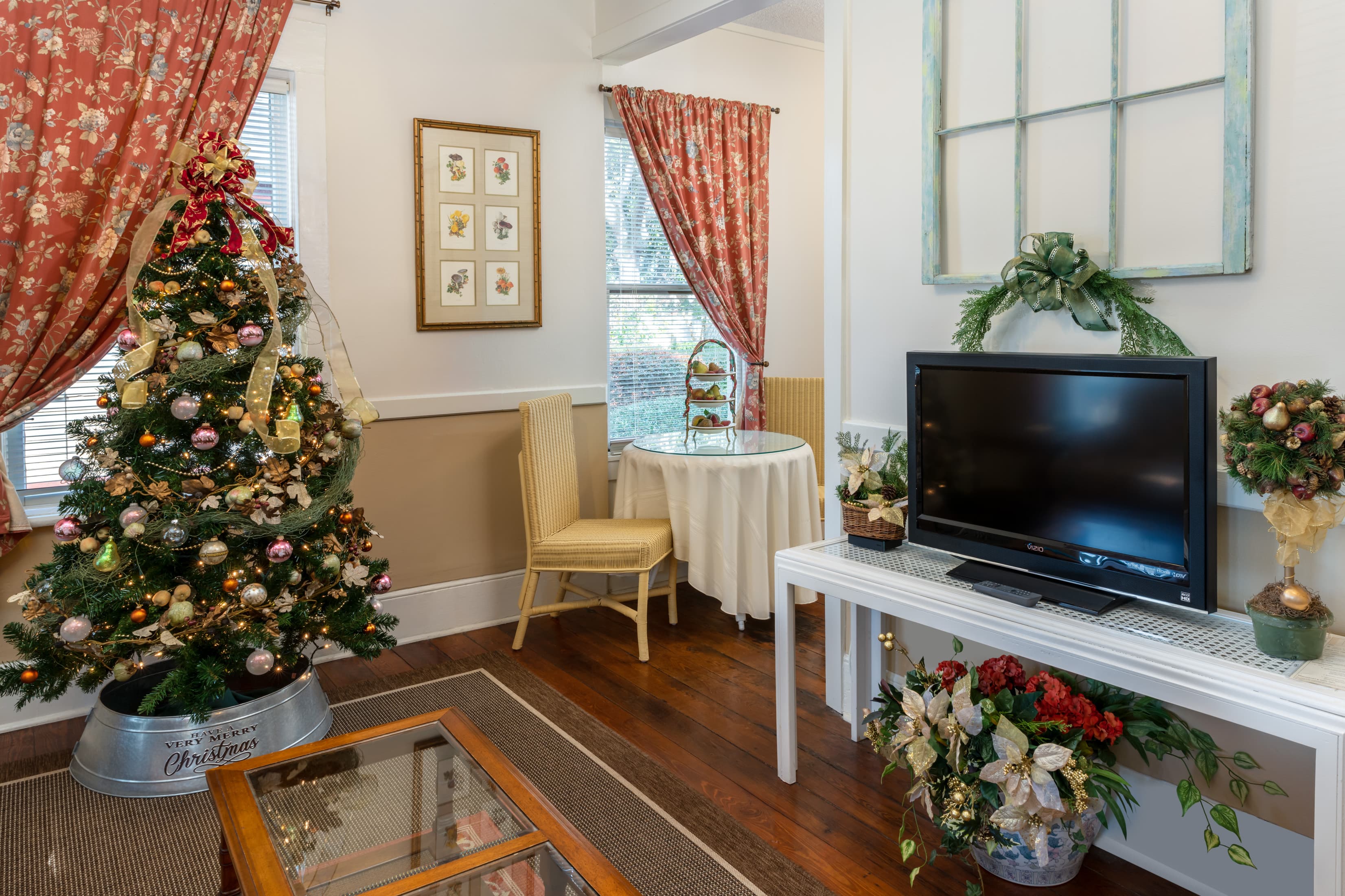Festively decorated living area showcasing a Christmas tree, vintage décor, hardwood floors, and comfortable seating with a cozy holiday atmosphere.
