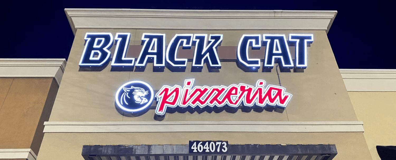Neon sign for "Black Cat Pizzeria" on a storefront at night.