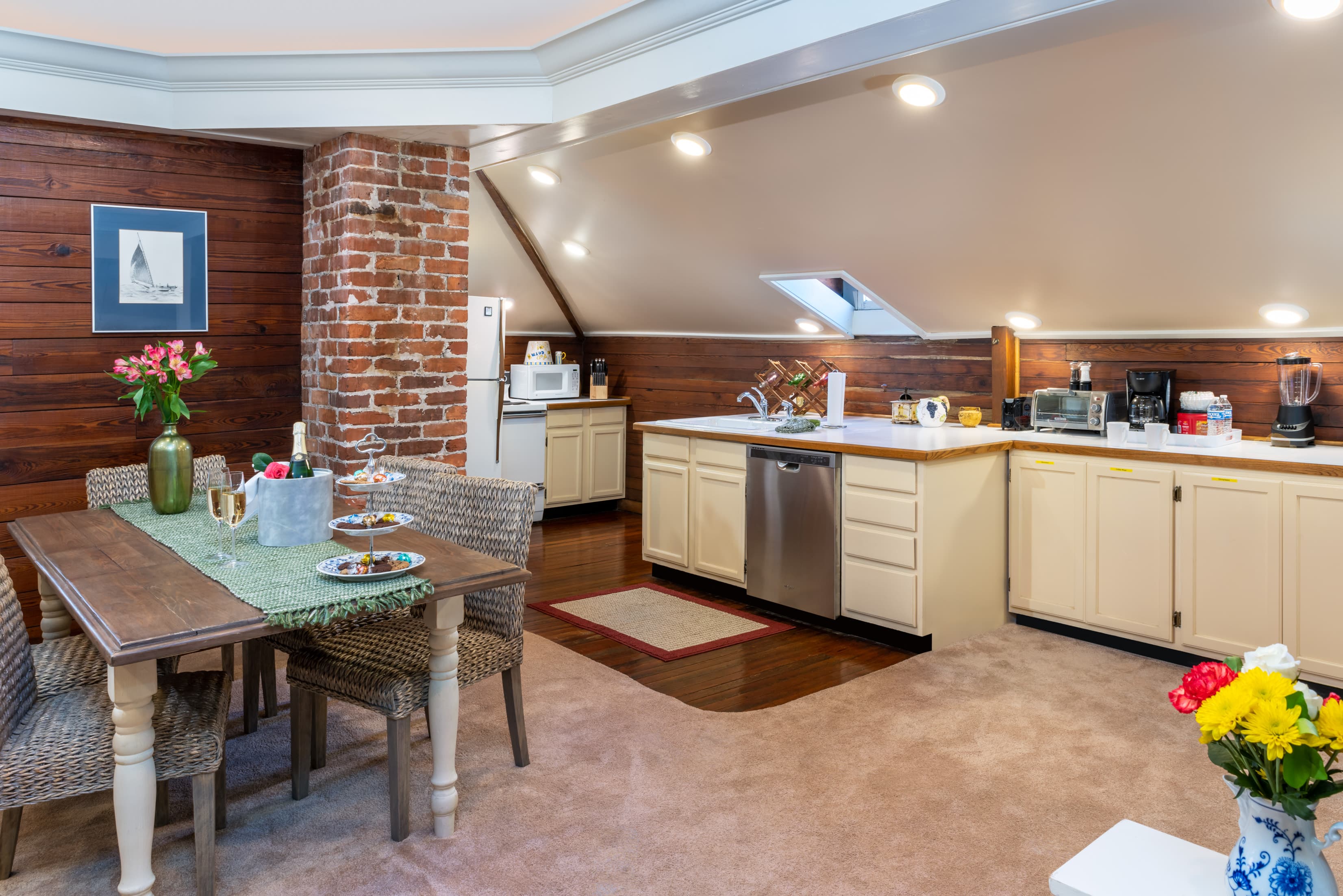 Spacious loft suite kitchen and dining area with vaulted ceilings, exposed brick, full kitchenette, dining table, and inviting open-concept layout.