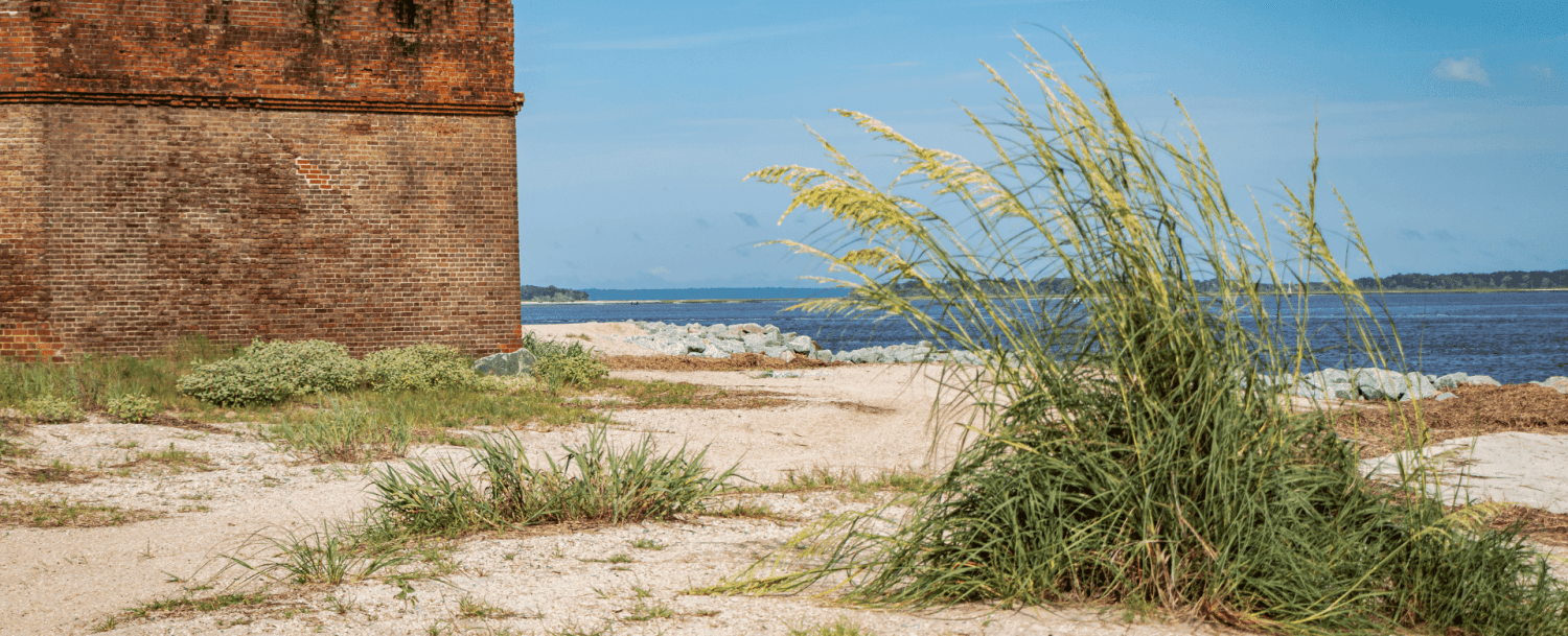 A brick structure stands near a grassy shoreline overlooking a calm body of water.