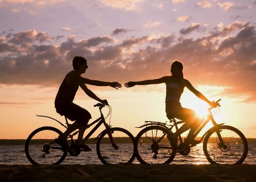 Couple riding bikes and reaching to hold hands along the beach at sunset near Amelia Island Couple riding bikes and reaching to hold hands along the beach at sunset near Amelia Island
