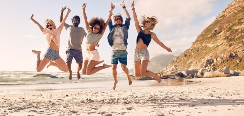 Group of friends jumping in the air together on a sandy beach near the ocean.
